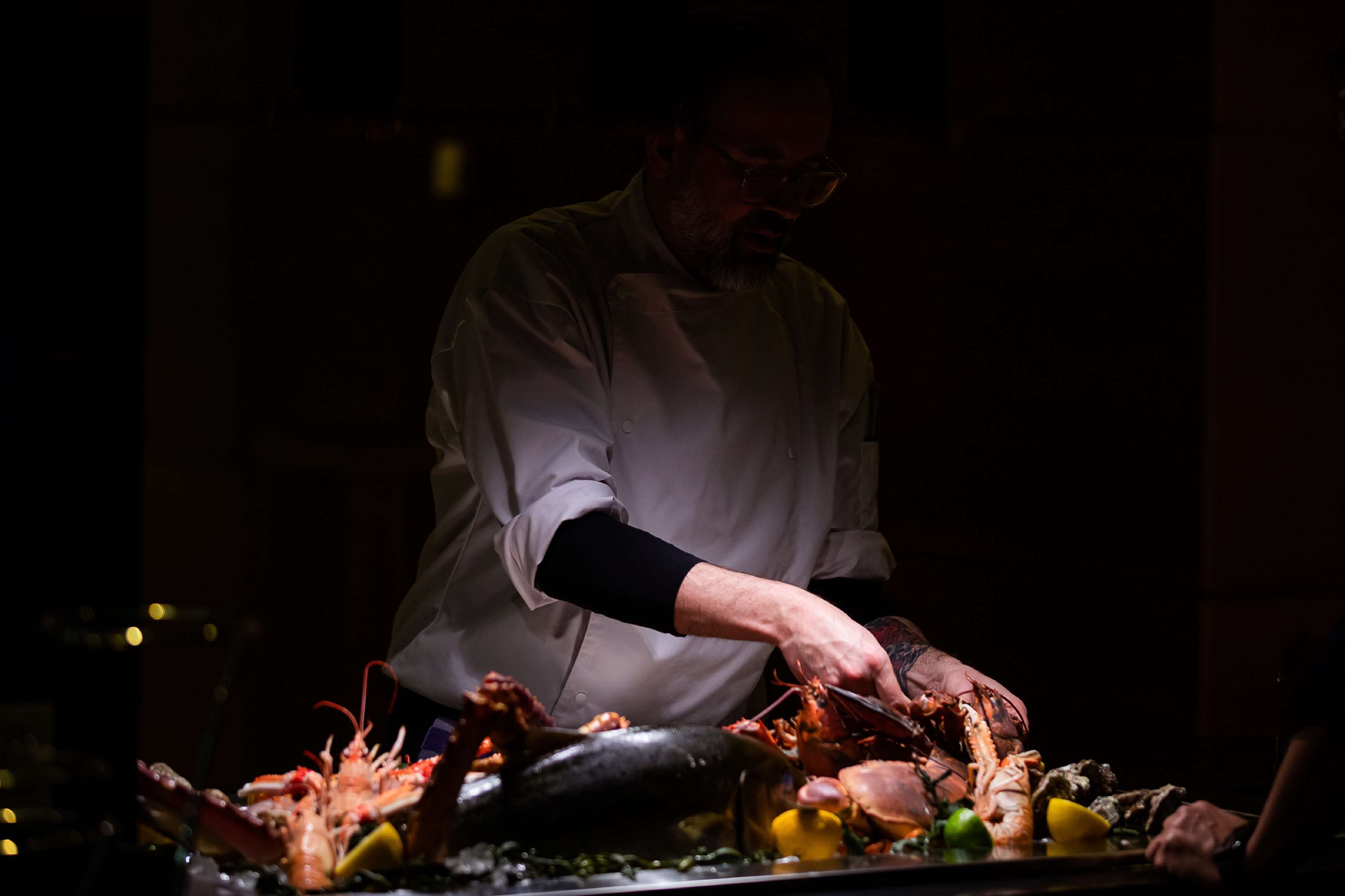 Um cozinheiro preparando frutos do mar em uma cozinha com pouca luz.