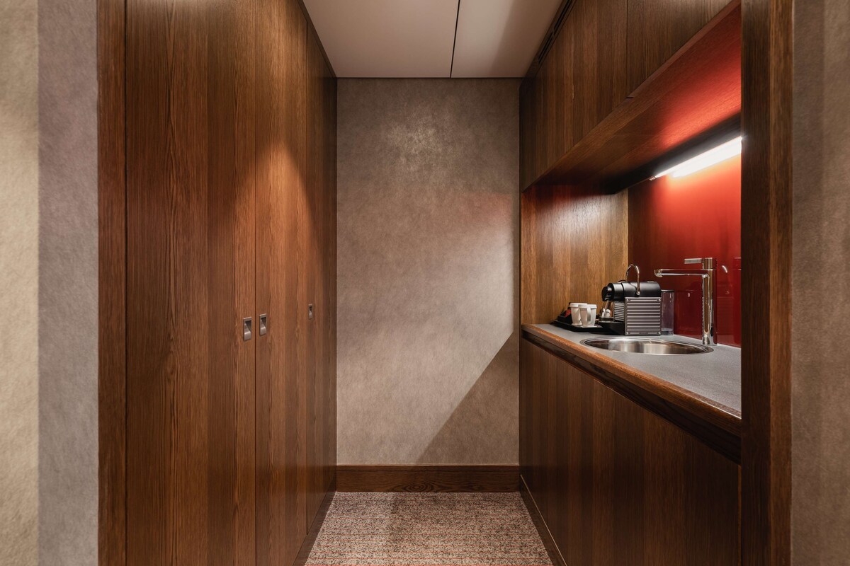 A narrow hallway with wooden cabinets and a small kitchenette area with a sink and coffee machine.