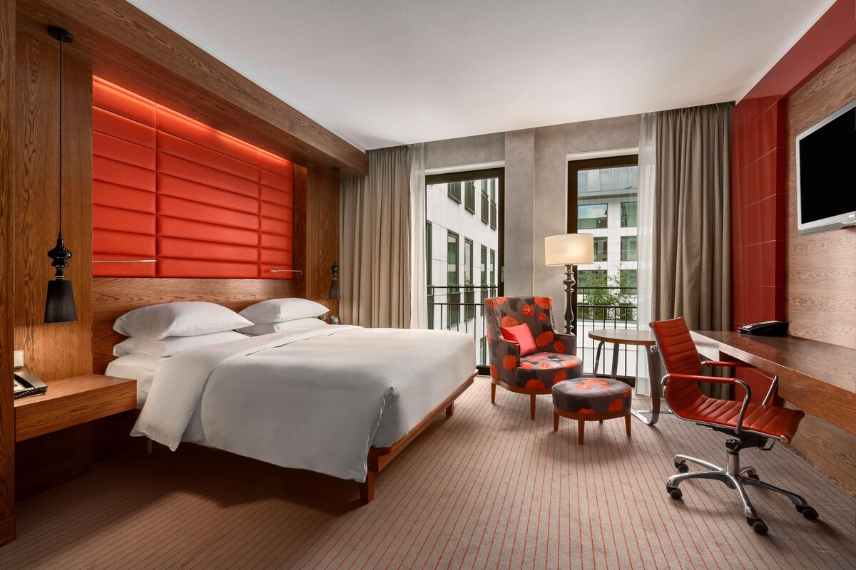 Hotelkamer met een groot bed, een bureau met stoel, een televisie en een raam met gordijnen.
