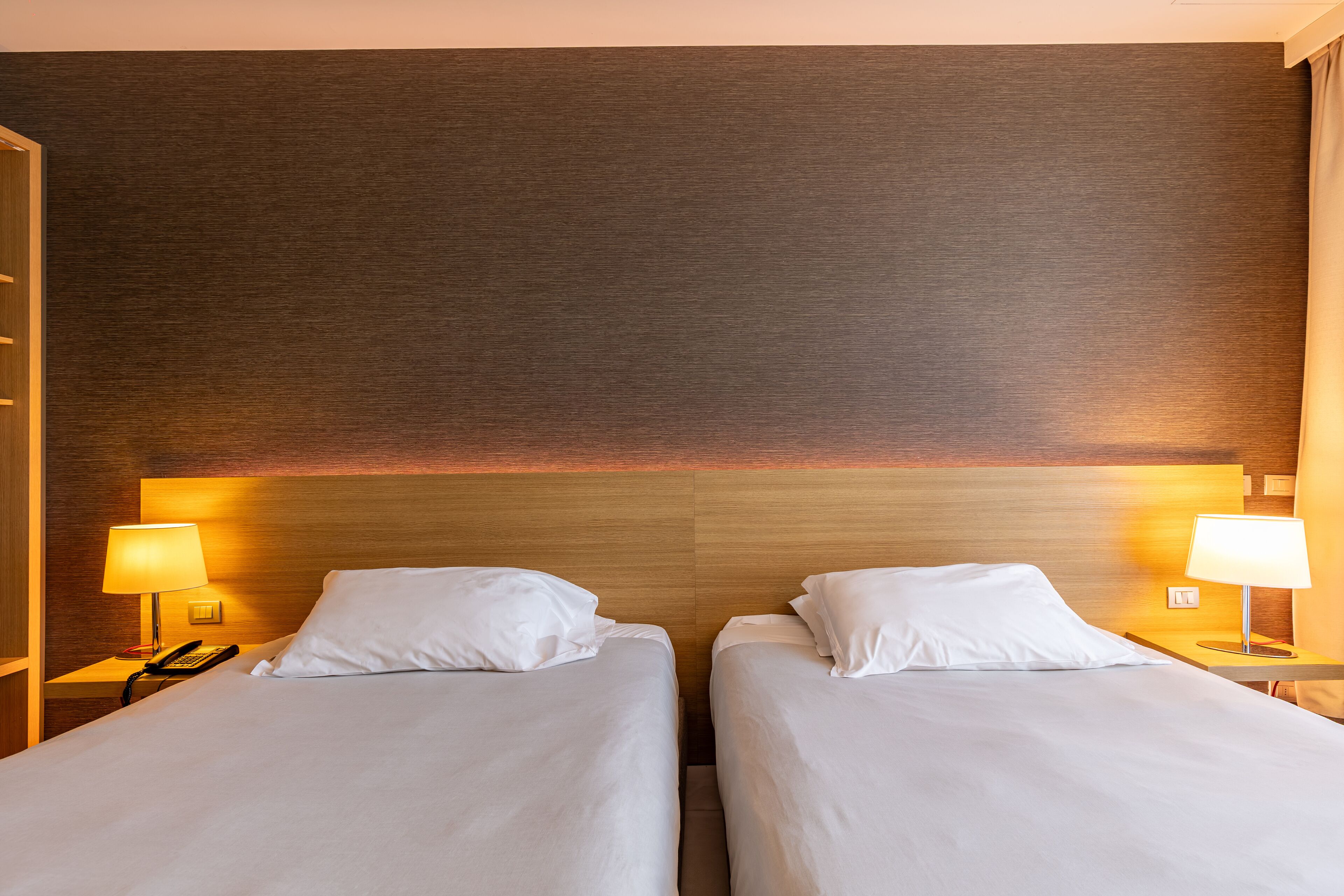 A hotel room with two beds, each with white linens and pillows, a wooden headboard, and bedside lamps.
