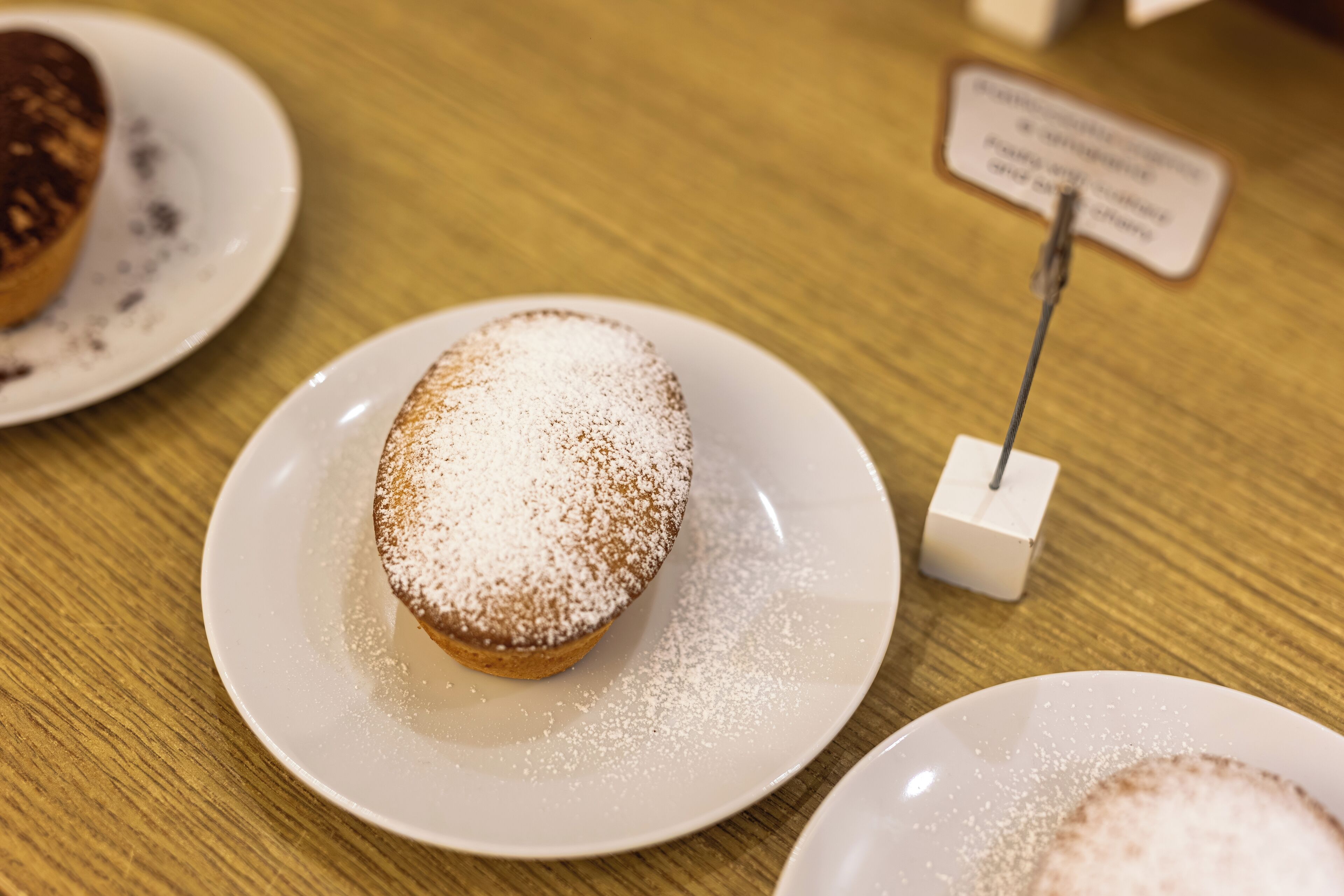 Un postre sobre un plato blanco, con azúcar glas, sobre una mesa de madera.