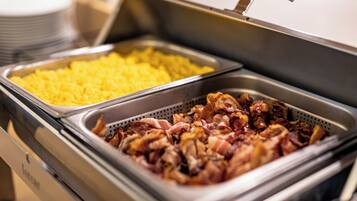 Un buffet con due vassoi di cibo: uno con uova strapazzate e l'altro con pancetta.