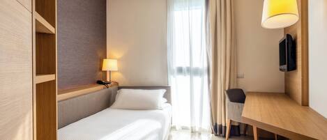 Een hotelkamer met een bed, nachtkastje, lamp en een bureau met stoel.