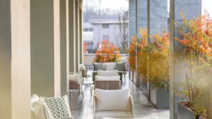 A covered outdoor seating area with white chairs and tables, potted plants, and a view of the city. - HSM Hotel San Martino (Garbagnate Monastero)