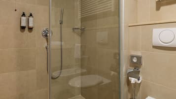 A modern bathroom with a glass-enclosed shower, a toilet, and a towel dispenser.