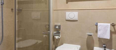 Un baño moderno con ducha envuelta en vidrio, inodoro y lavamanos pedestal.
