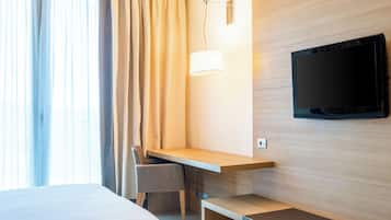 Habitación de hotel con cama, escritorio, silla, televisor montado en la pared y ventana con cortinas.