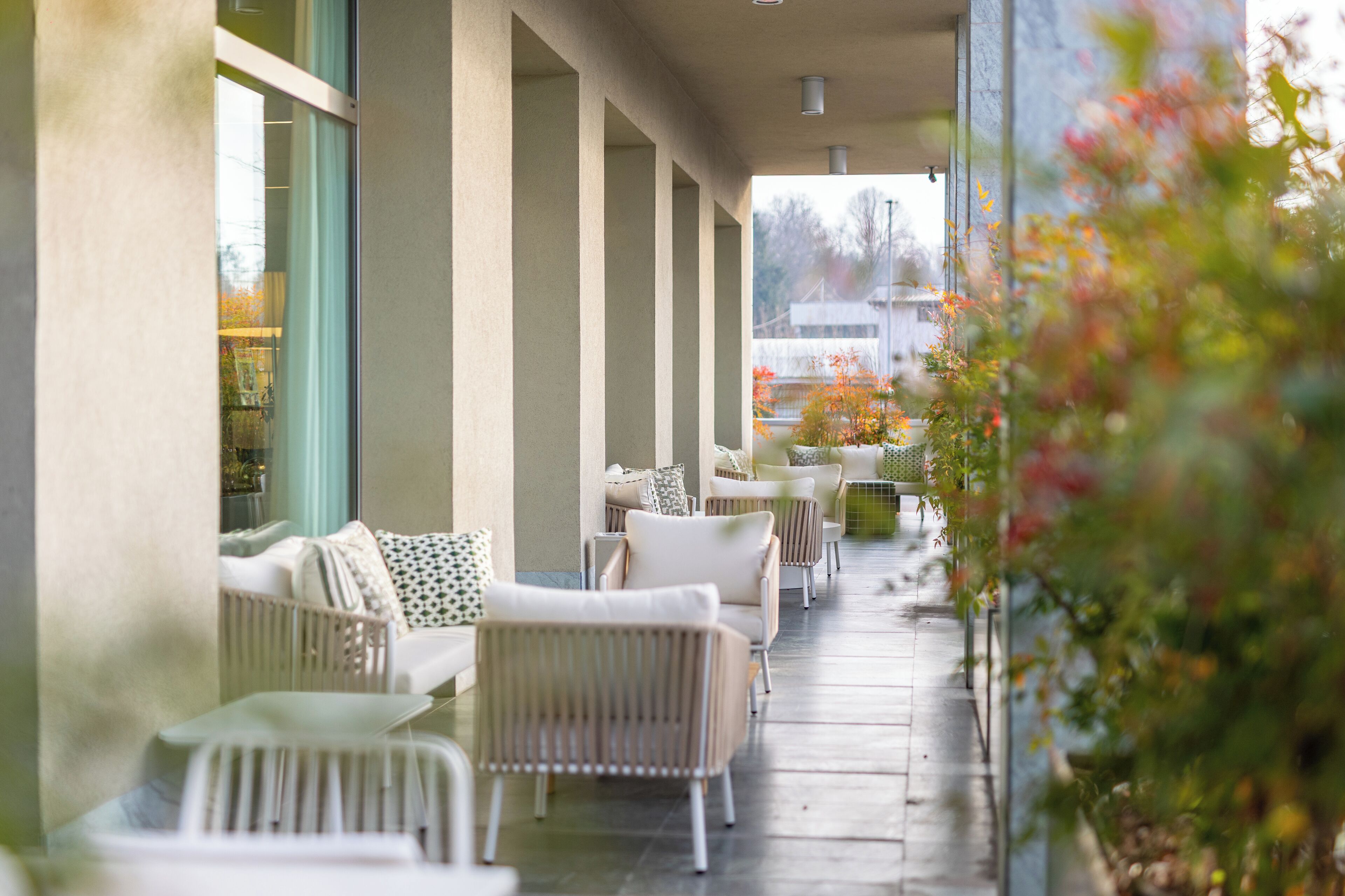 A covered outdoor seating area with white wicker furniture and a view of a building in the background.