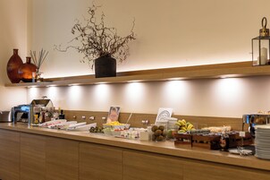 Montaje de bufé con diversos alimentos, una planta decorativa y una máquina de café.