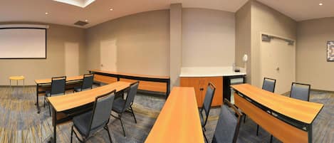 A conference room with a long table, chairs, a projector screen, and a carpeted floor.