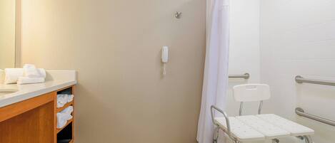 A bathroom with a shower, a toilet, a sink with a towel rack, and a wheelchair-accessible bench.