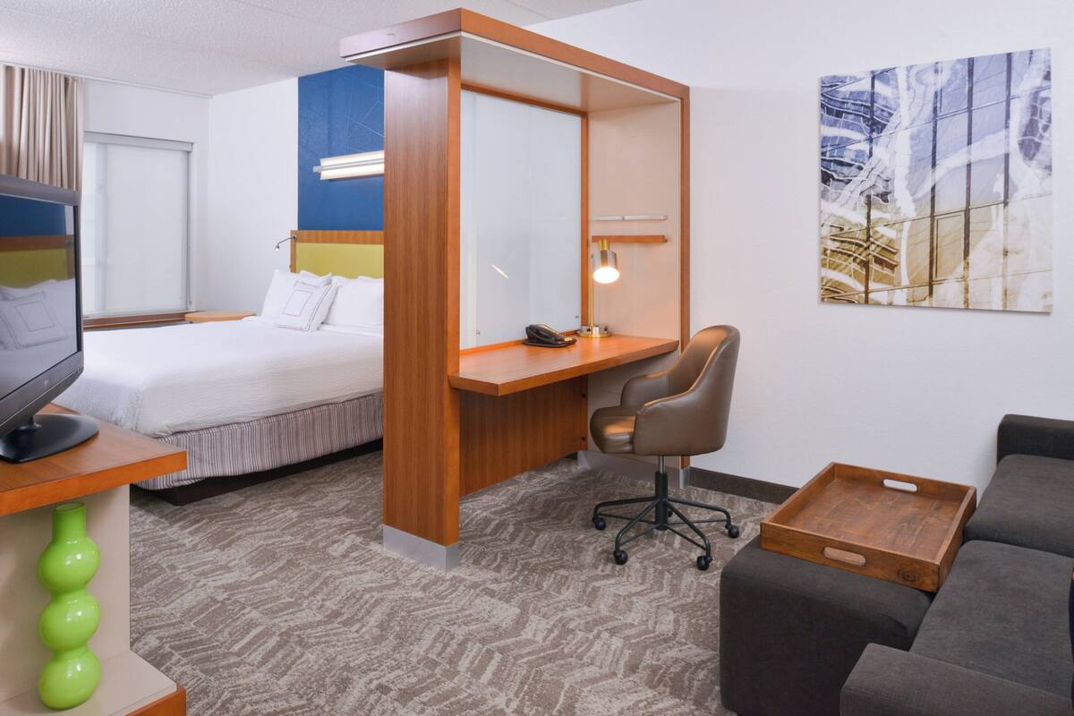 A hotel room with a bed, desk, chair, and a sofa.