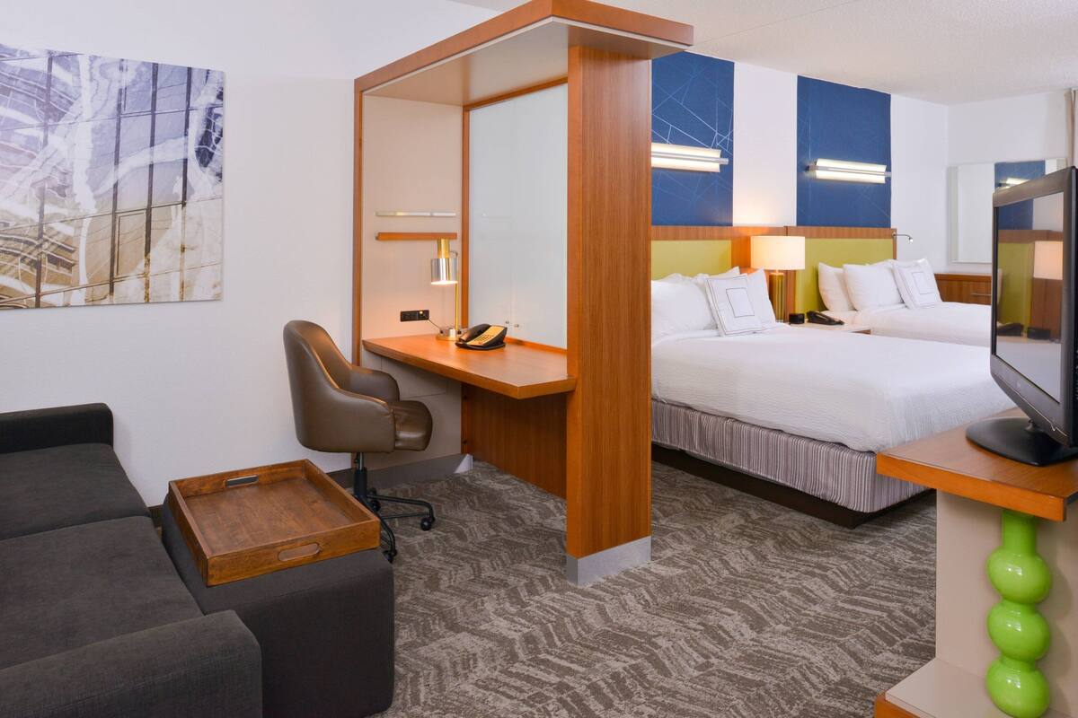 A hotel room with a bed, a desk with a chair, a small sofa, and a TV.