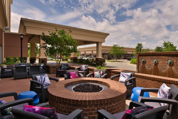An outdoor patio area with a circular brick fire pit, wicker furniture, and a covered seating area under a pergola. - SpringHill Suites by Marriott Durham Chapel Hill (Durham)