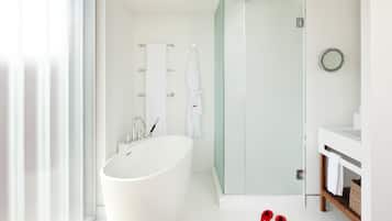 Een moderne badkamer met een vrijstaand bad, een douche met glazen wanden en een witte wastafel met spiegel.