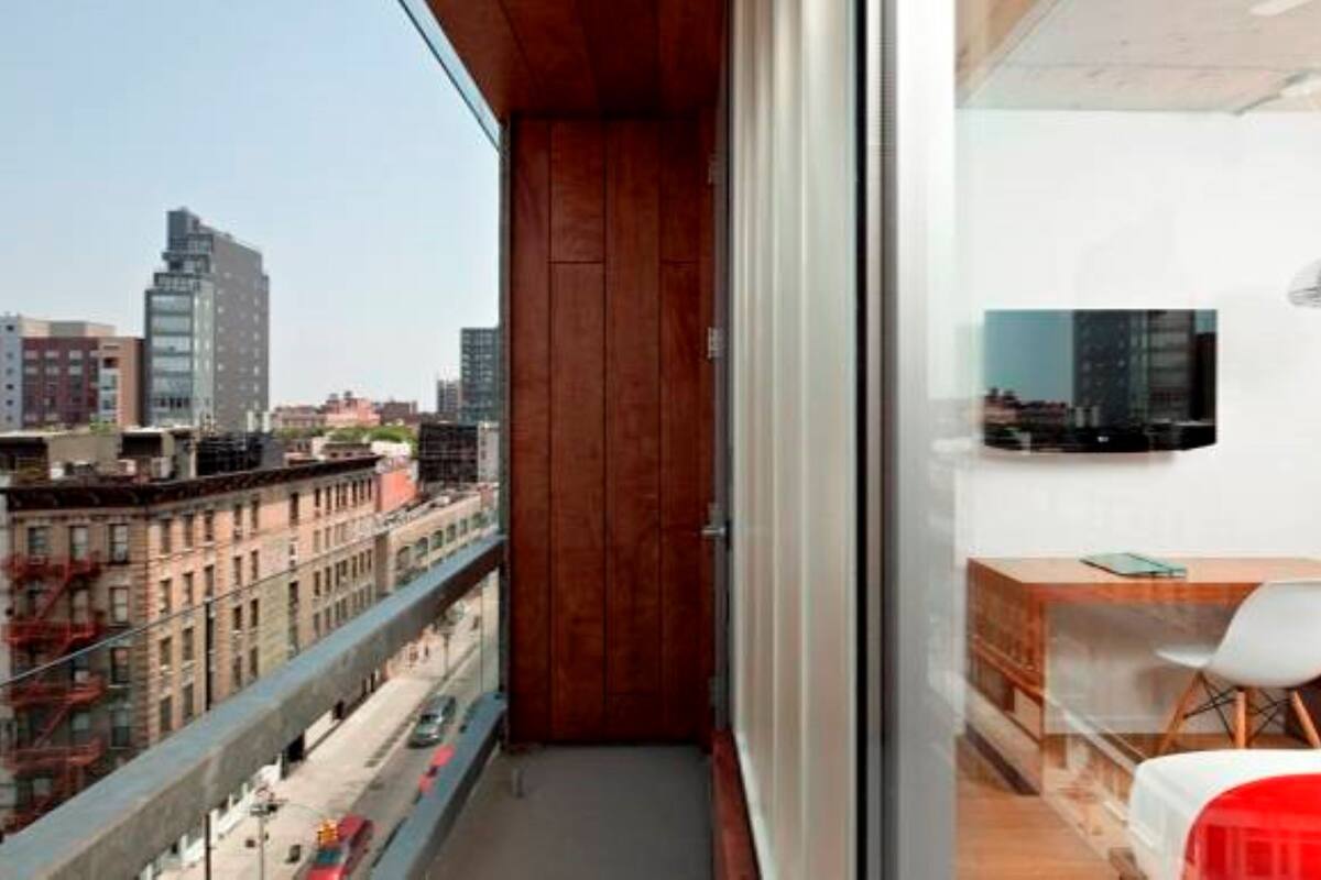 Un apartamento moderno con vistas a la ciudad, un balcón de madera, un escritorio pequeño con una silla y un televisor montado en la pared.