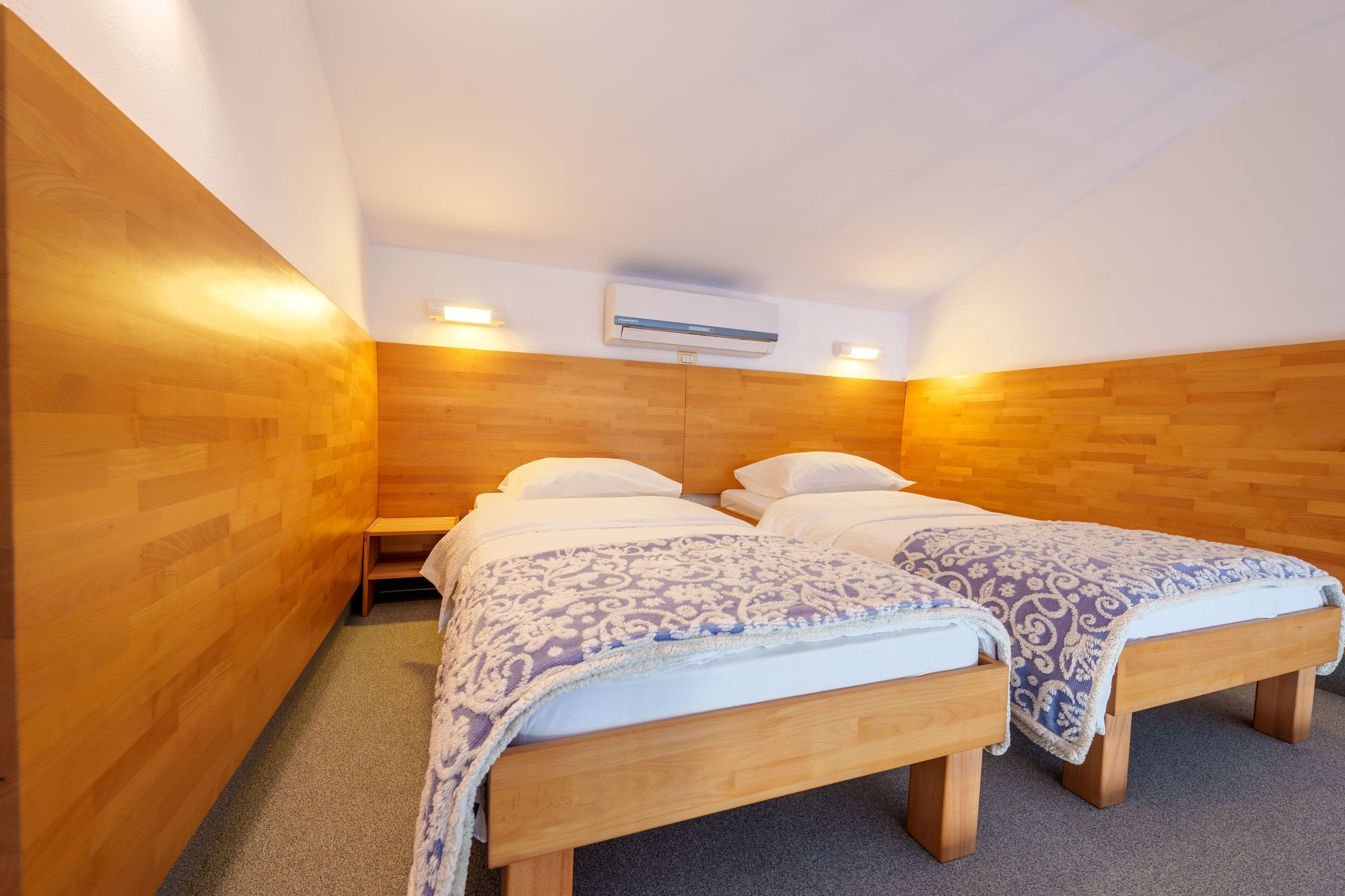 A room with two wooden beds, a ceiling fan, and a wall-mounted air conditioner.