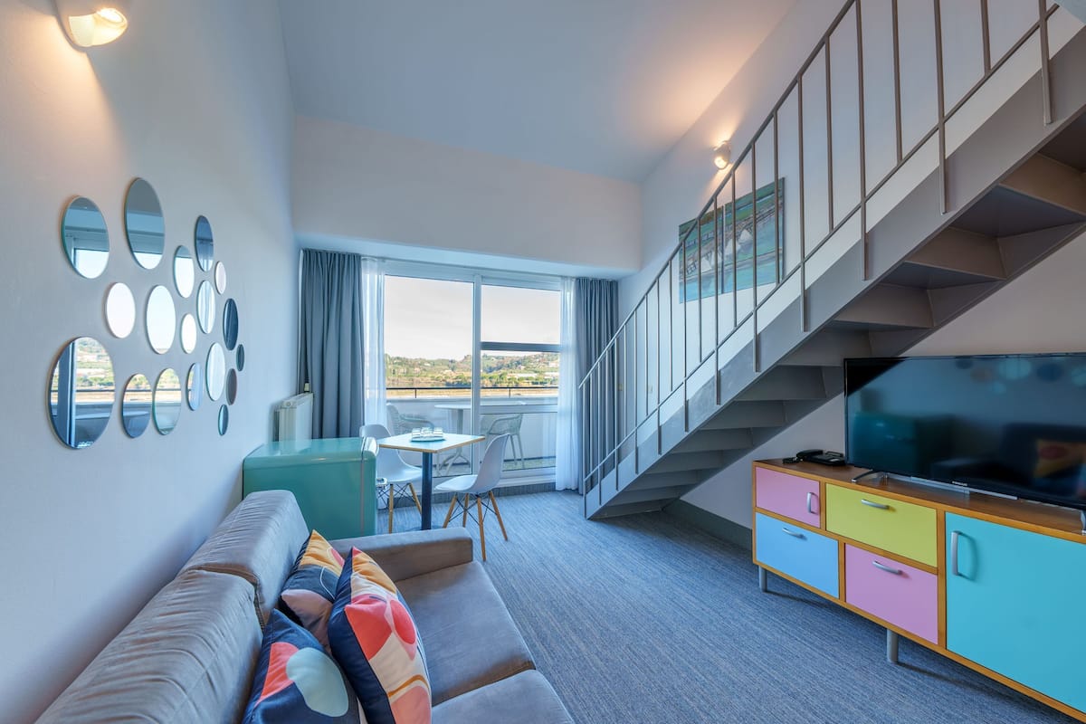 A modern living room with a sofa, a TV, a staircase, and a balcony with a view.