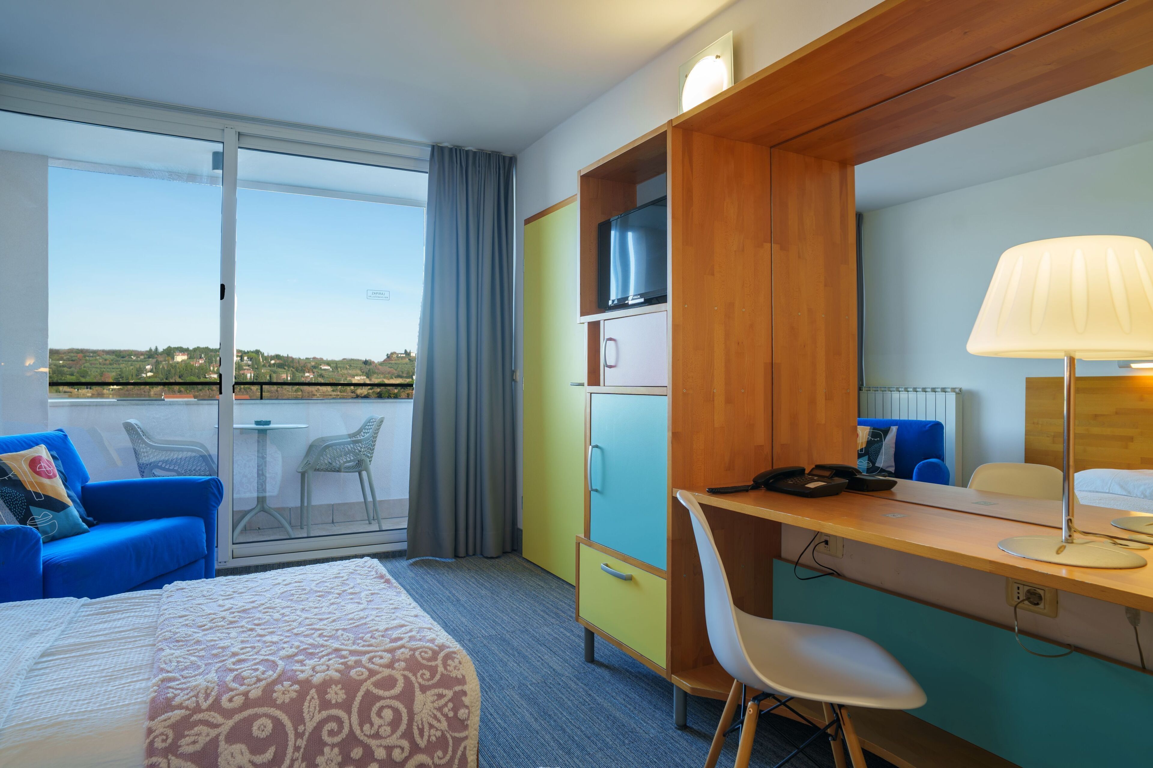 Una habitación de hotel con cama, escritorio, silla, televisión y vistas al exterior.