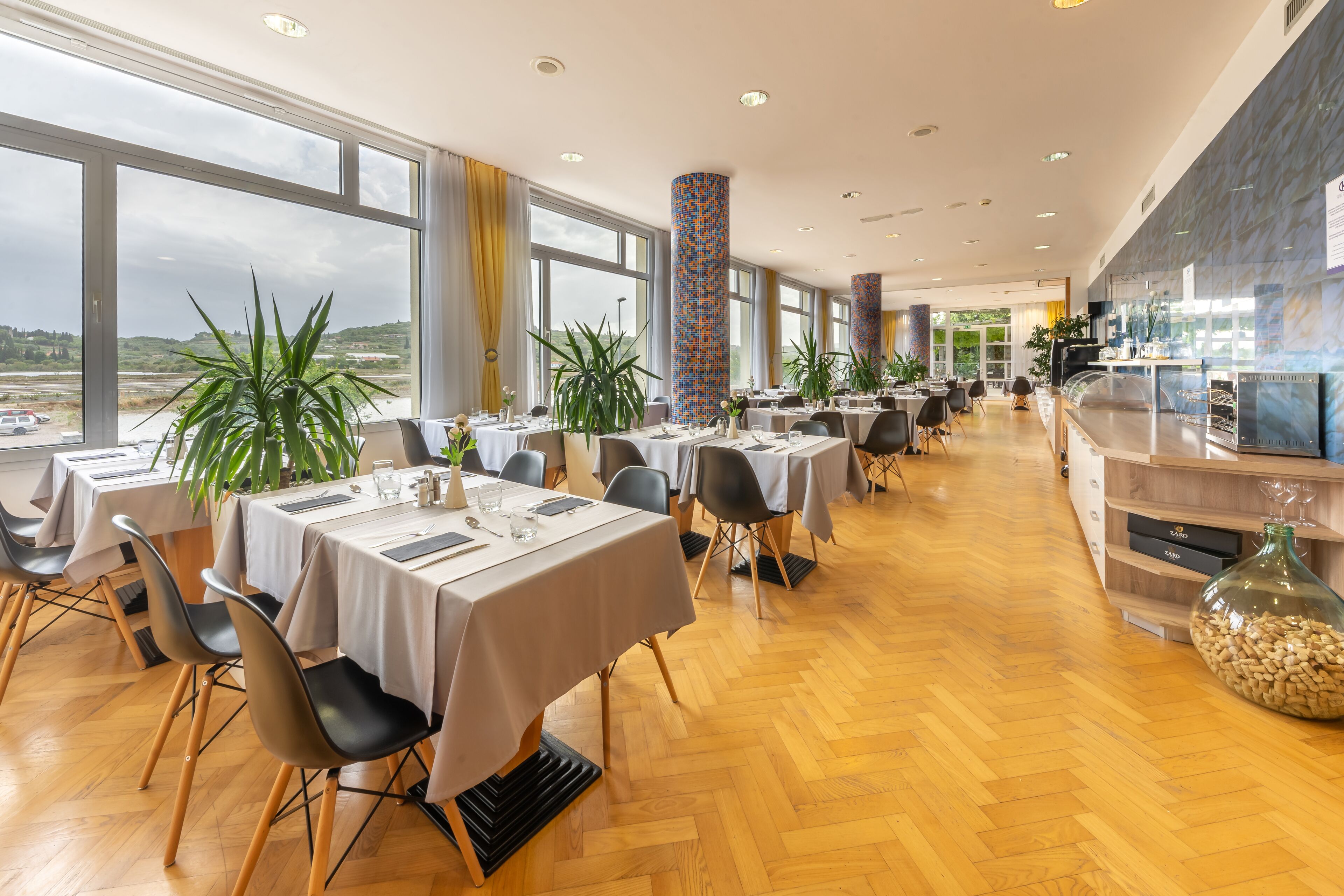 Un comedor amplio con varias mesas y sillas, ventanas grandes que ofrecen vistas al paisaje, y un diseño interior moderno.