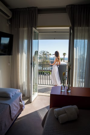 A hotel room with a bed, a desk with a vase, and a view of the outside. - Fantini Club Hotel  (Cervia)