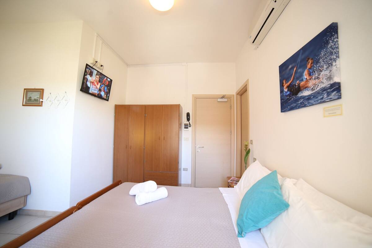 A neatly arranged bedroom with a bed, a wooden wardrobe, a television mounted on the wall, and a framed picture.