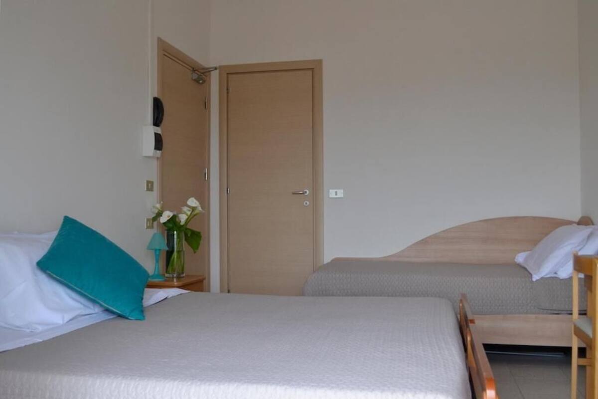 A room with two beds, a wooden door, and a small table with a vase of flowers.