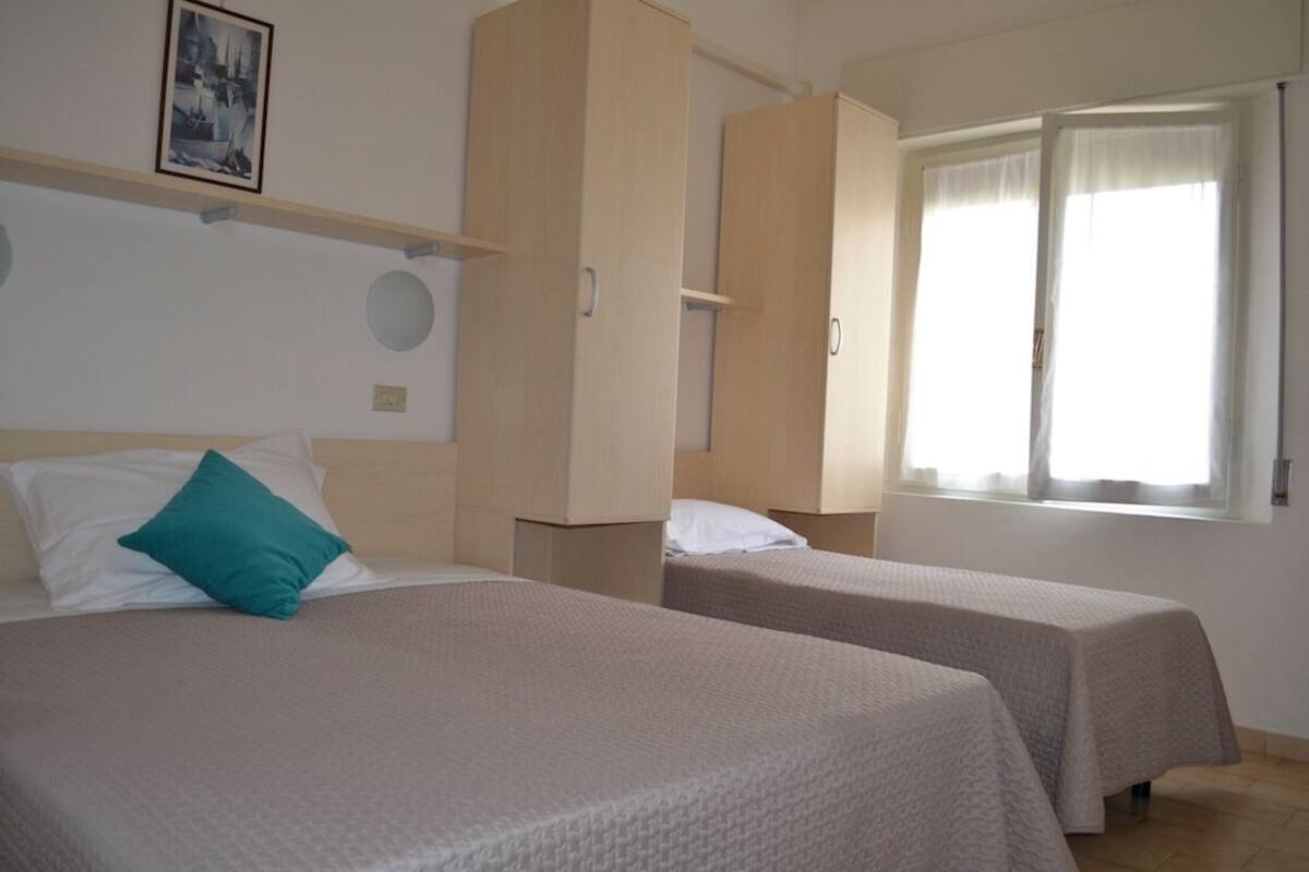 A room with two beds, a wardrobe, a window with curtains, and a picture on the wall.