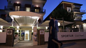 The entrance of Sportur Club Hotel with a covered entrance, a signboard, and a person walking in front. - Fantini Club Hotel  (Cervia)