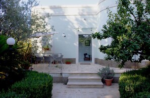 A white building with a glass door, a patio with chairs, and potted plants.