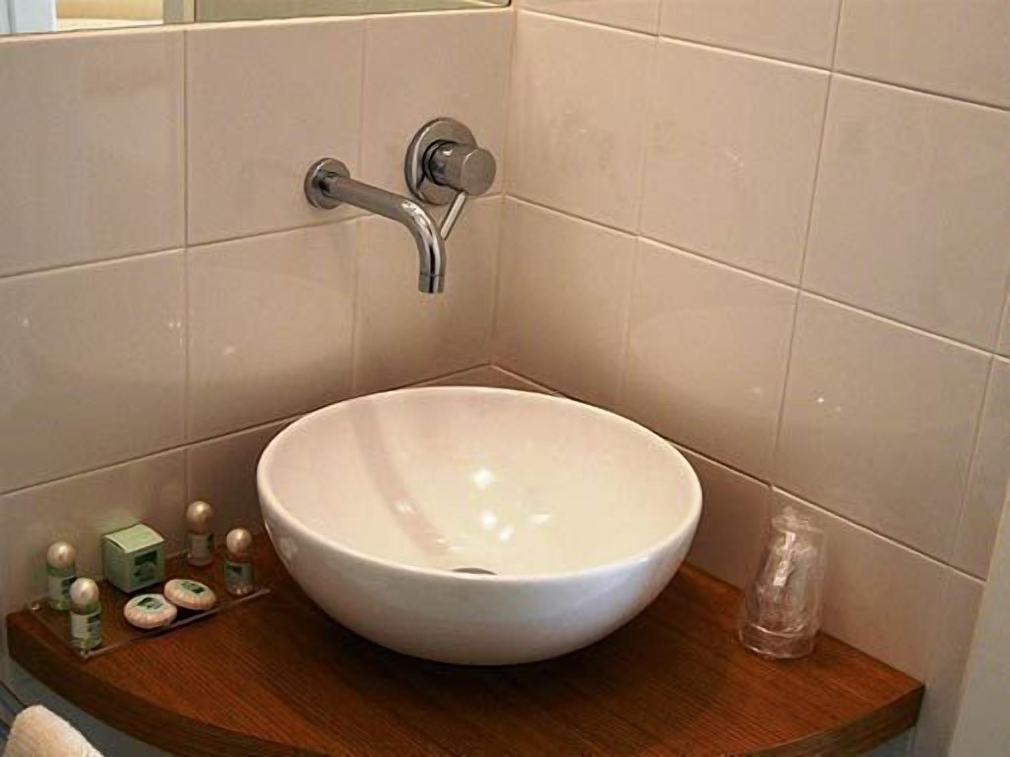 Un bagno con lavandino bianco, mobiletto in legno e articoli da toilette sul ripiano.