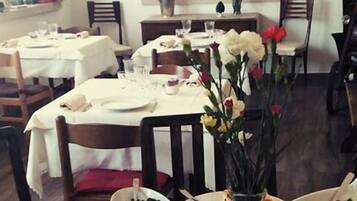 Comedor con varias mesas dispuestas para una comida, una bodega en el fondo y un jarrón con flores sobre la mesa.