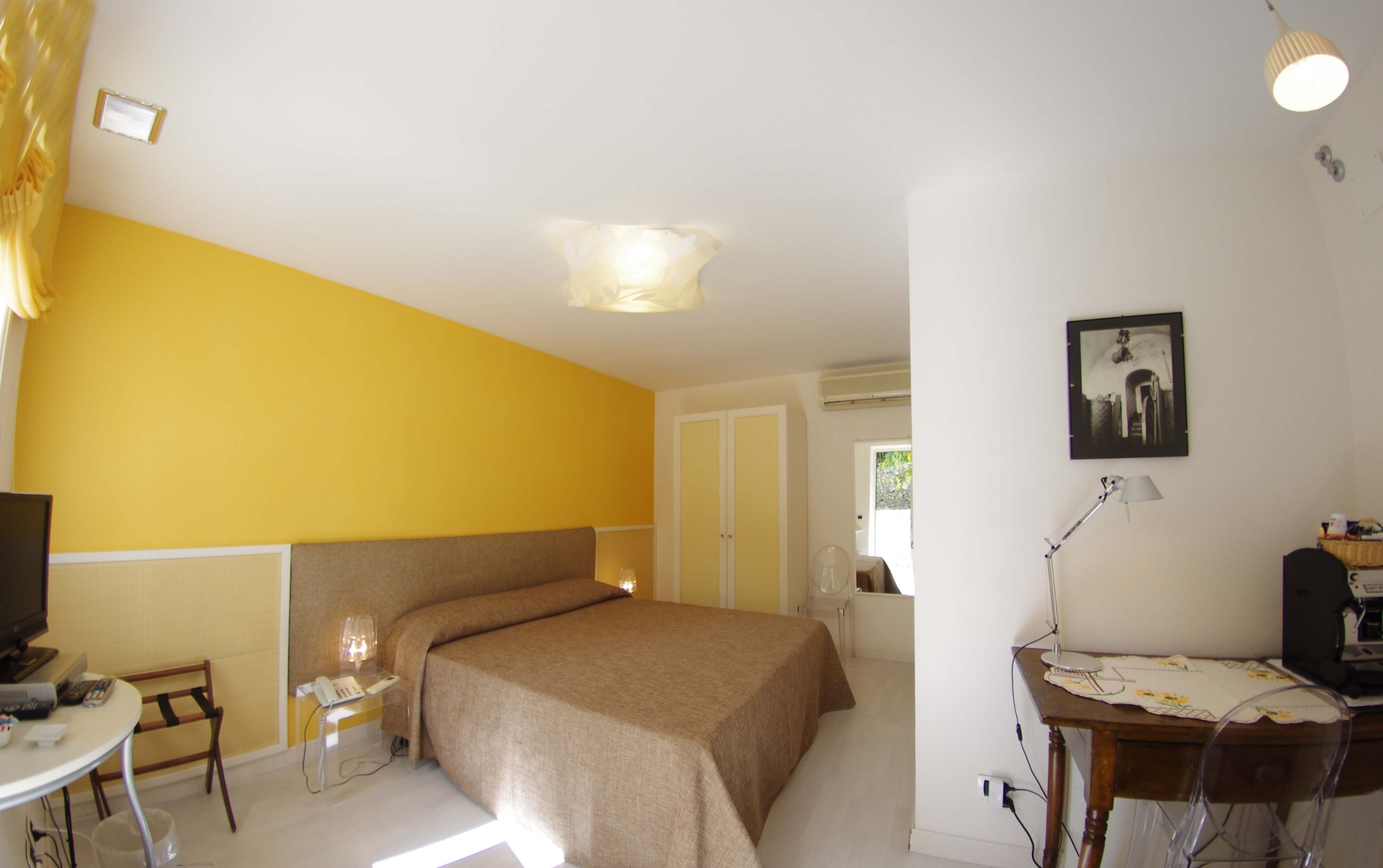 A hotel room with a bed, a desk with a lamp, a chair, a television, and a picture on the wall.