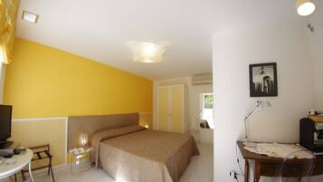 A hotel room with a bed, a desk with a lamp, a chair, a television, and a picture on the wall.