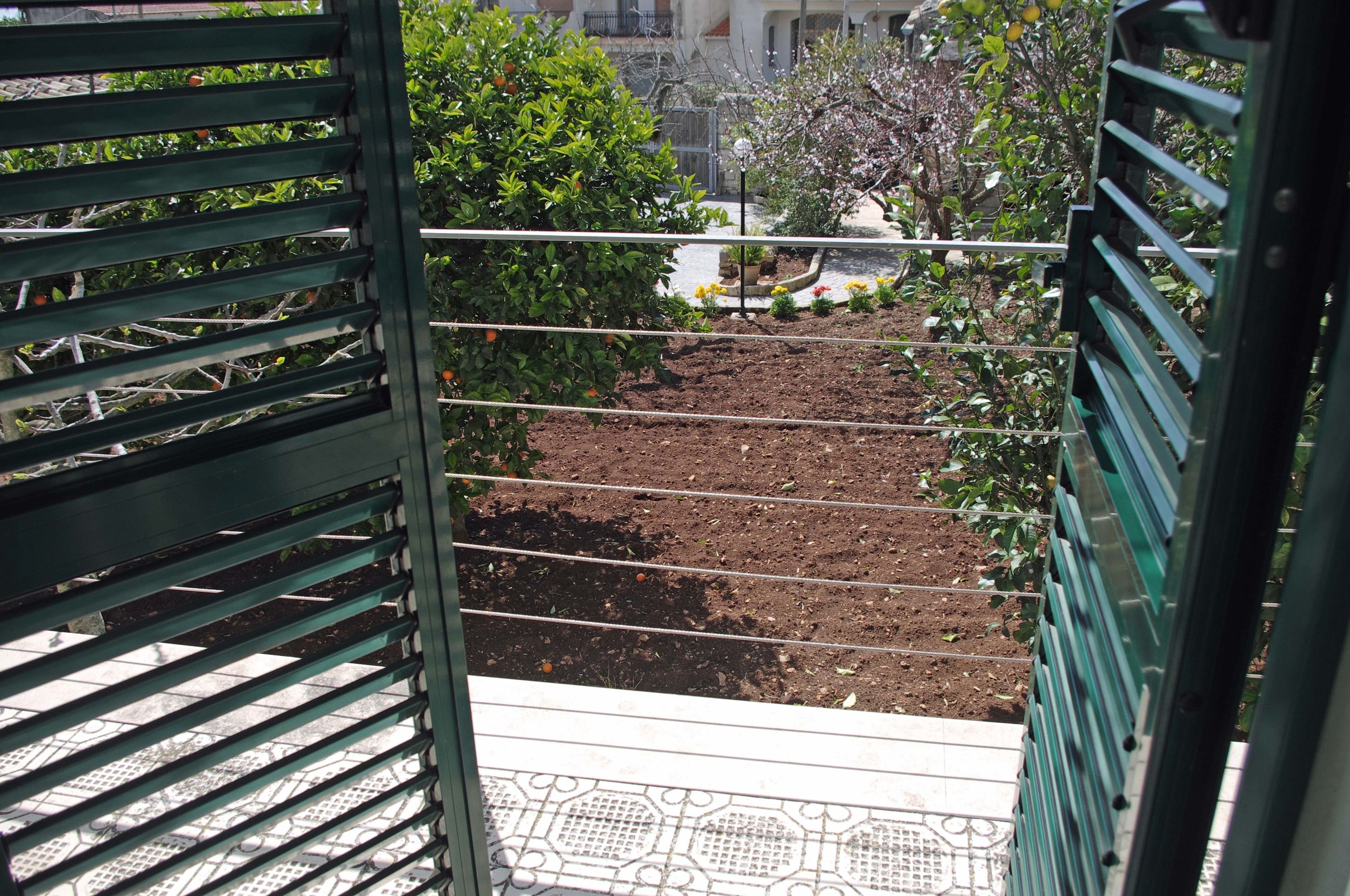 A balcony with a view of a garden, metal railings, and a patterned floor.