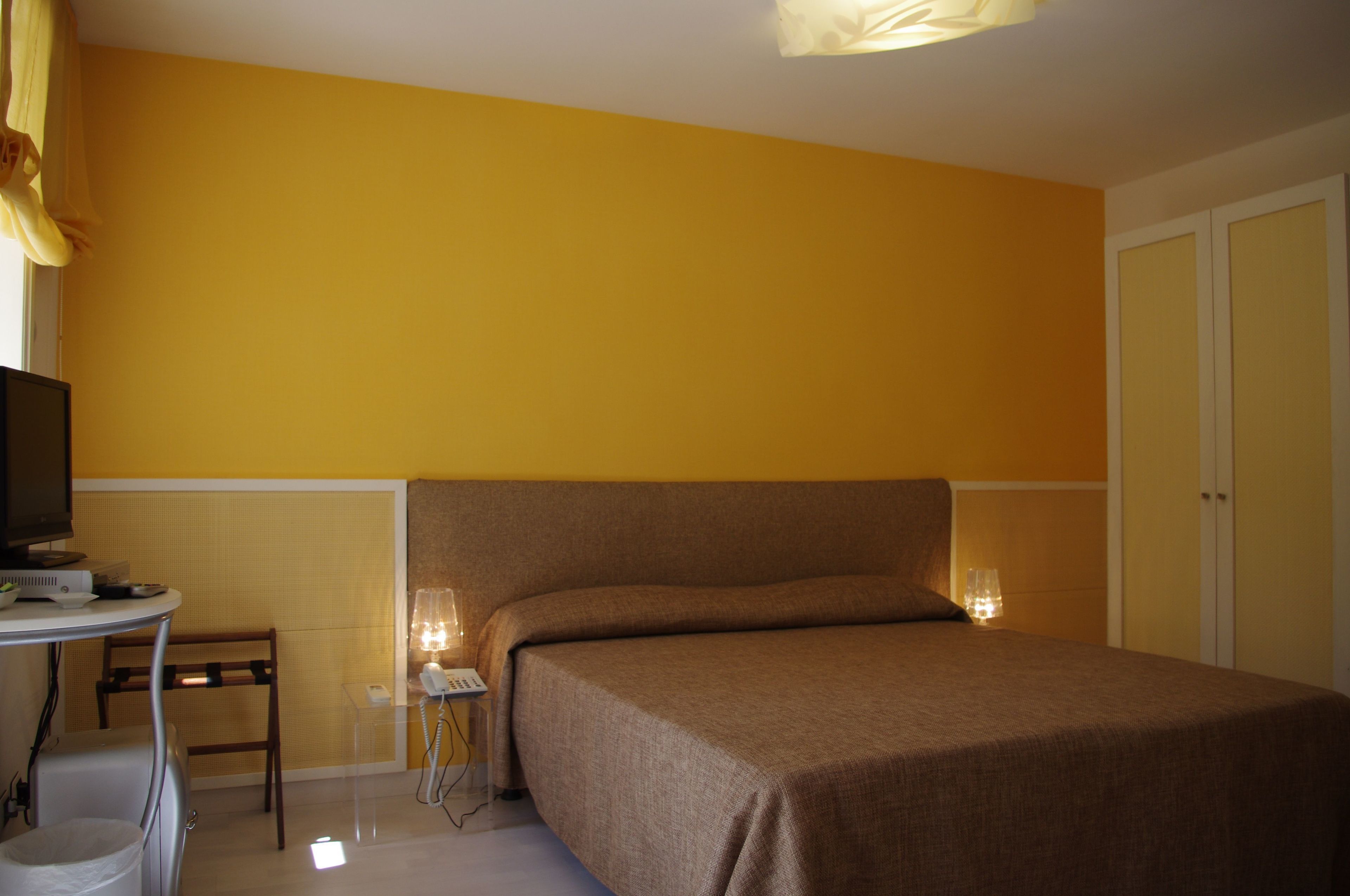Una stanza con un letto, una scrivania con una lampada e una televisione.