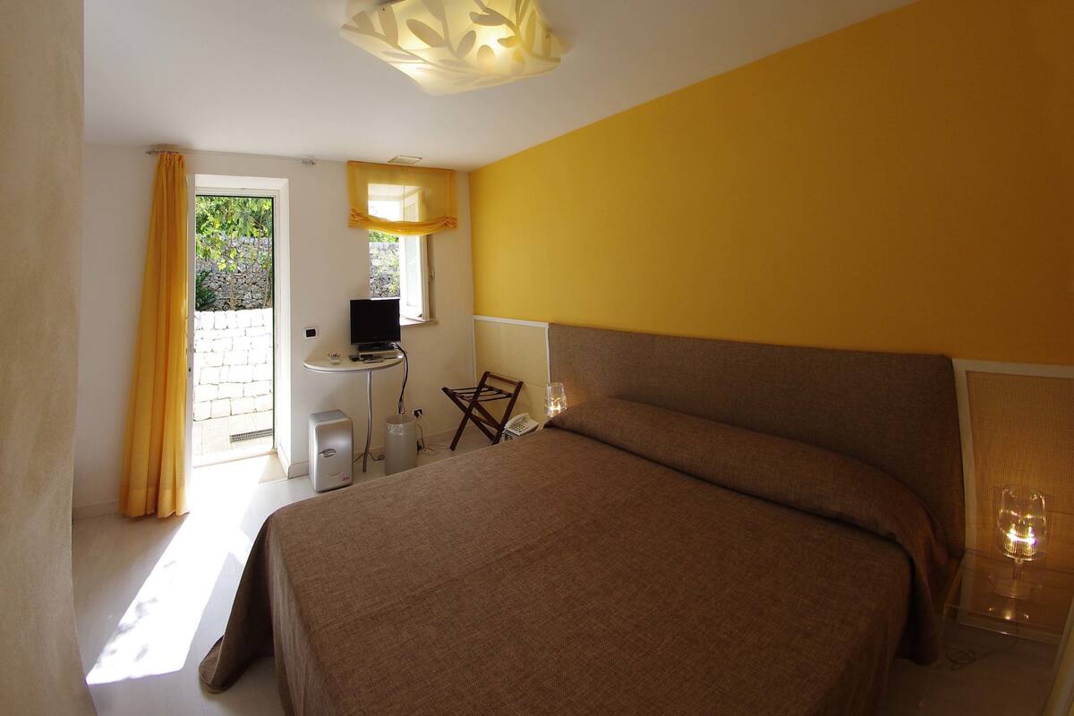 Habitación de hotel con cama, una mesita de noche con televisor, una silla y una ventana con cortinas.