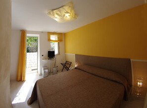 A hotel room with a bed, a small table with a TV, a chair, and a window with curtains.
