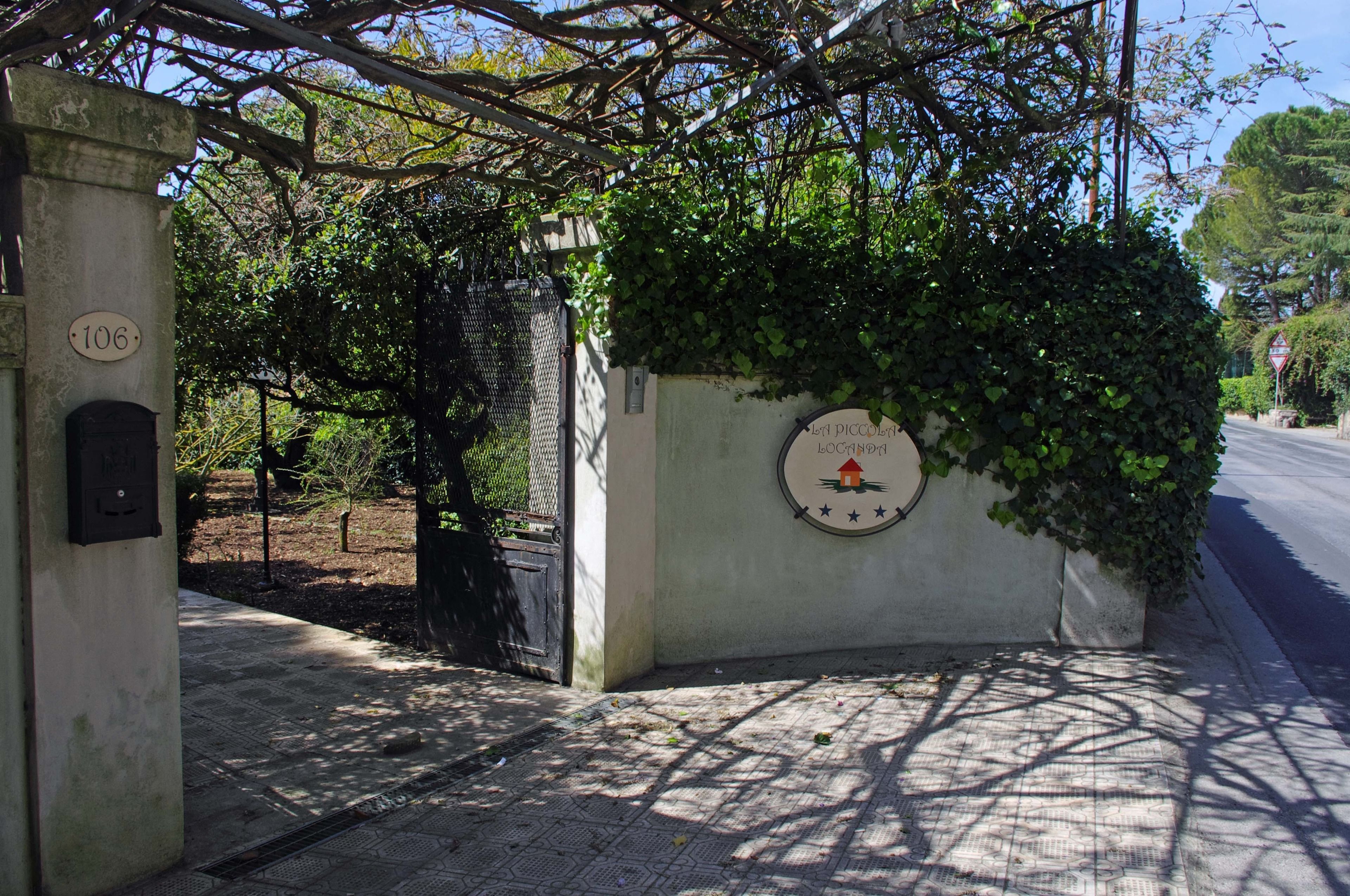 A building entrance with a concrete pillar marked '106', a metal gate, and a wall with a circular sign featuring a house and stars.