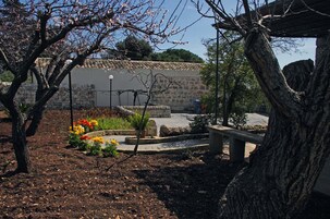 Um jardim com muro de pedra, um banco e plantas floridas.