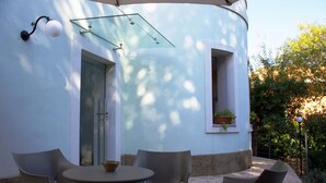 Un patio al aire libre con una mesa redonda y cuatro sillas, un ventanal y una ventana con una planta en maceta.