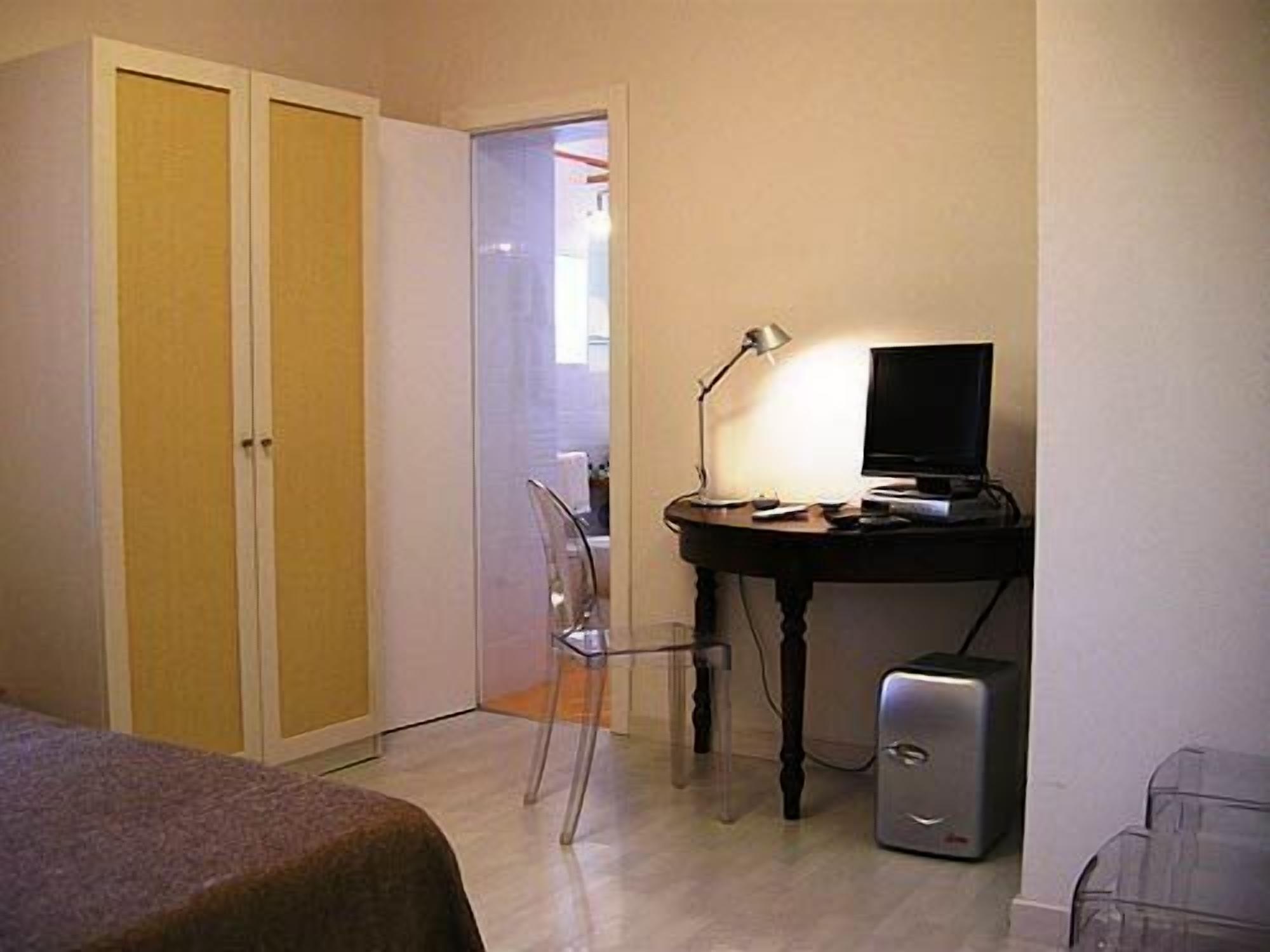 Een kleine kamer met een bureau, een stoel, een computer en een kledingkast.