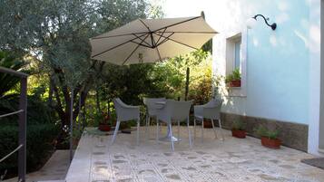 Terrassa exterior amb taula i cadires, un parasol gran i plantes en testos.