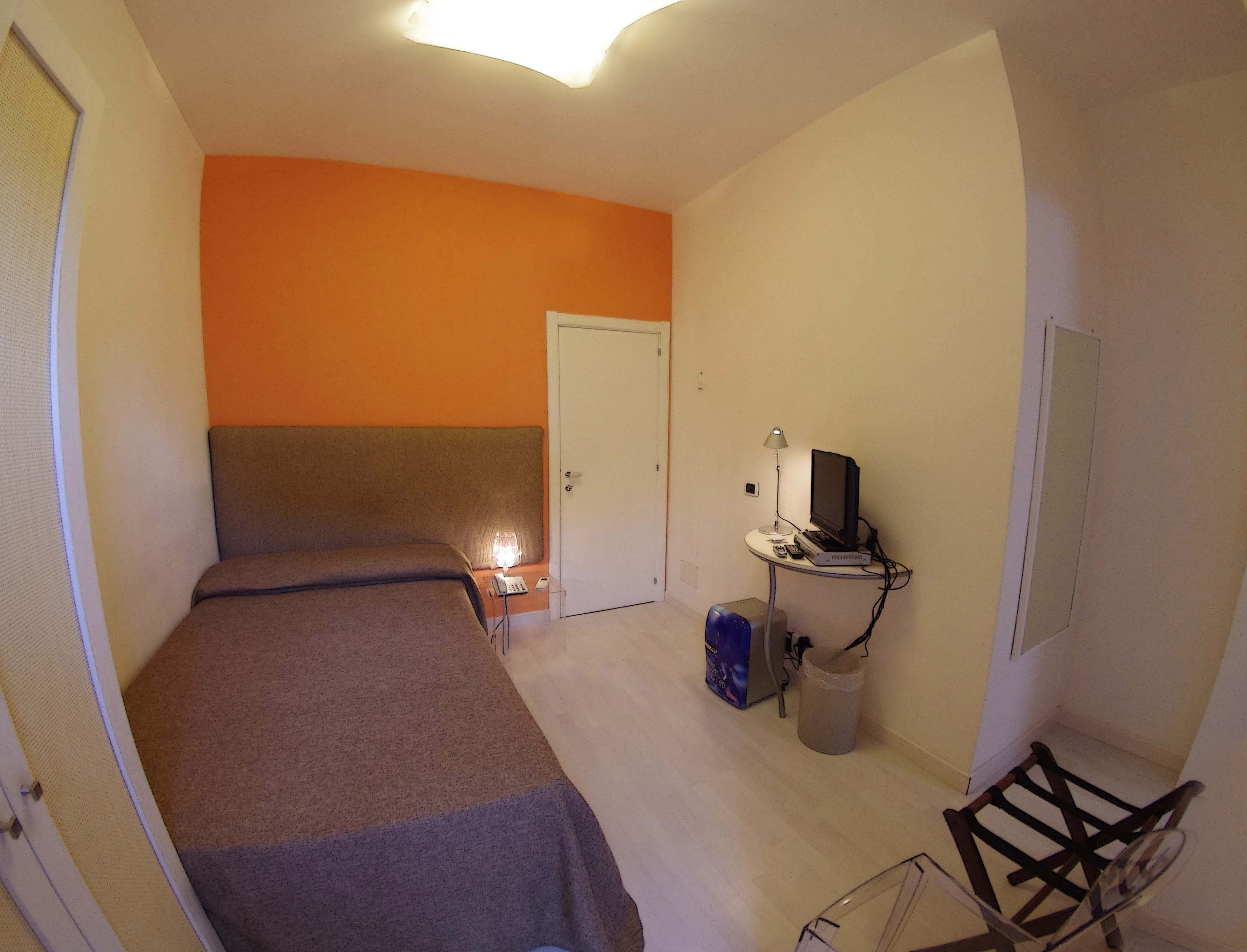 Una habitación con dos camas, un escritorio con computadora, una lámpara y un cesto de basura.