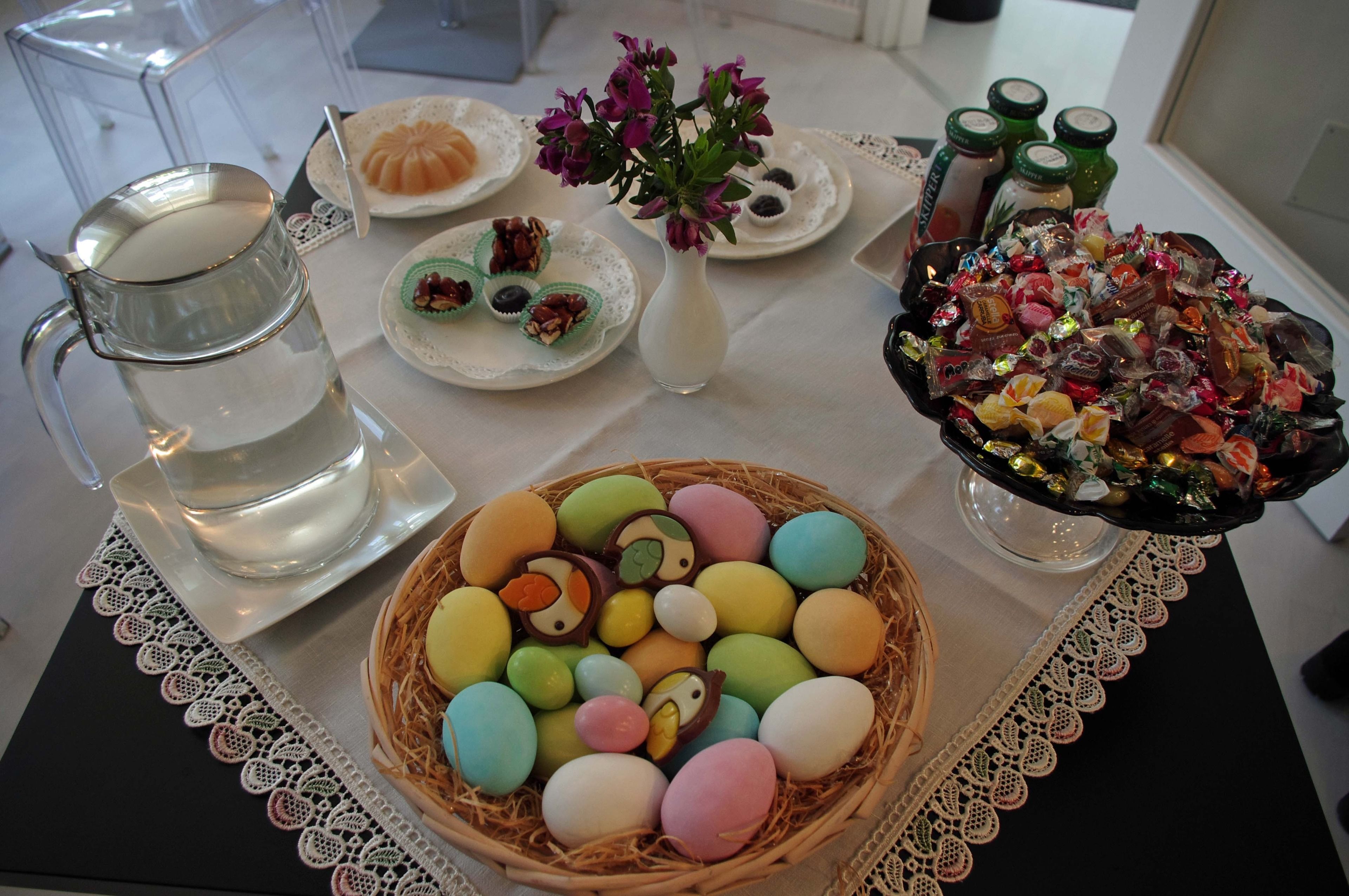 A table with a variety of food items, including a basket of colorful eggs, a pitcher of water, and a plate with pastries.