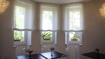 Quarto com uma mesa de jantar, cadeiras e três janelas com cortinas.