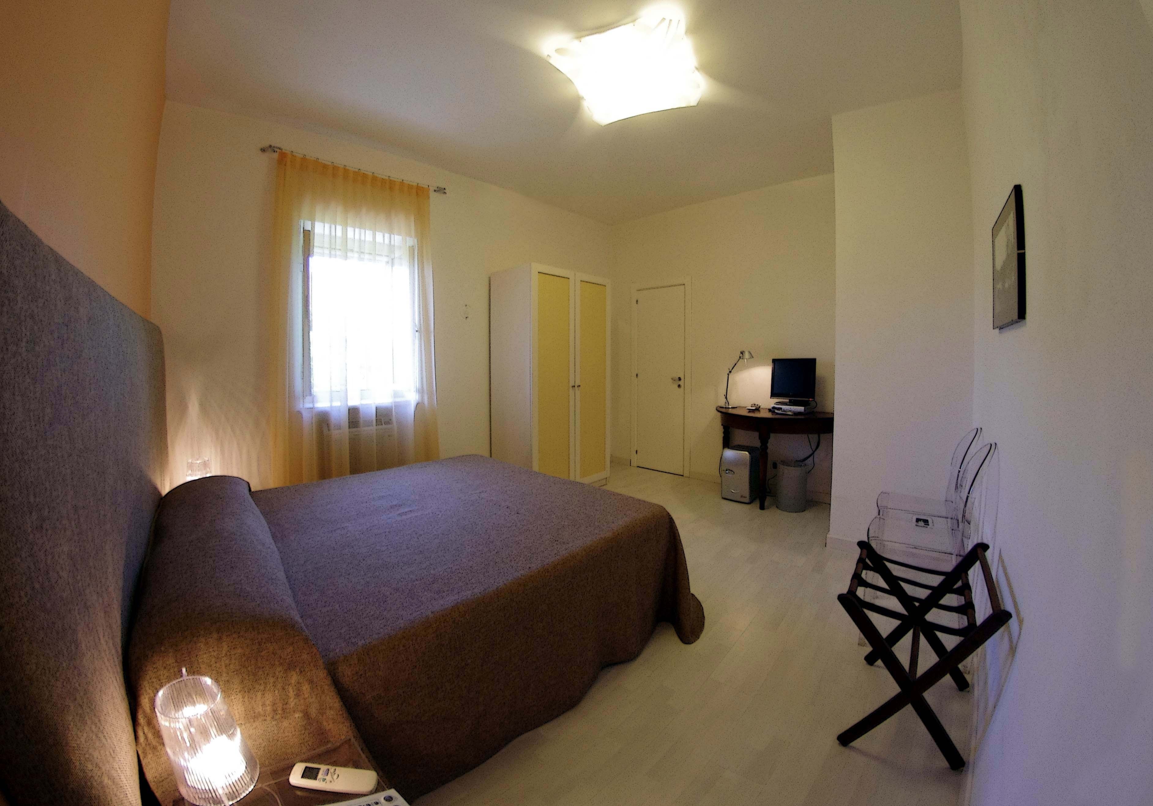 Una camera da letto con un letto, una scrivania, una sedia, una lampada e una finestra con tende.