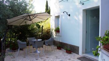 An outdoor patio with a table and chairs, surrounded by potted plants and a large umbrella.