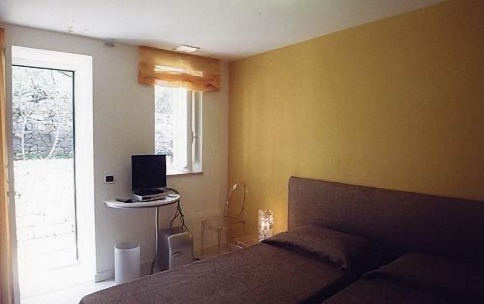 A bedroom with a bed, a desk with a computer, a window with a curtain, and a door leading to a balcony.