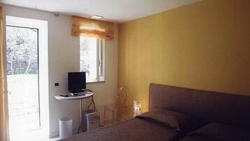 A bedroom with a bed, a desk with a computer, a window with a curtain, and a door leading to a balcony.